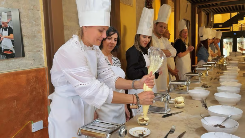 Partecipanti in grembiule bianco durante un corso di cucina a Roma imparano a preparare la pasta fatta in casa con macchine per la pasta su un bancone attrezzato