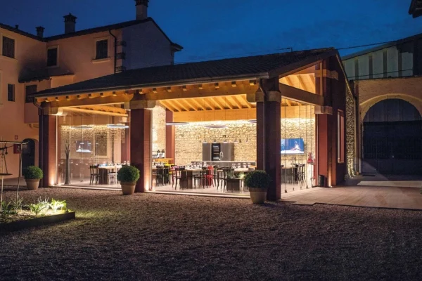 Vista notturna della Wine Boutique di Cantina Farina a Pedemonte di San Pietro in Cariano, con struttura in legno e vetro illuminata, tavoli apparecchiati per la degustazione e corte storica sullo sfondo, nel cuore della Valpolicella Classica